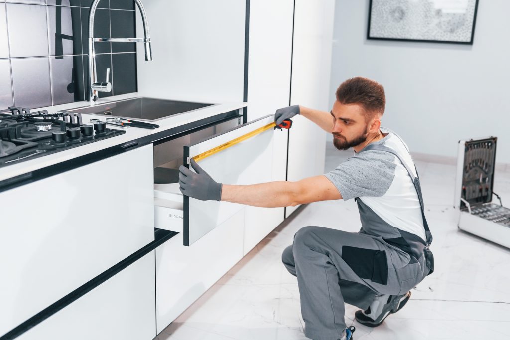 young professional plumber grey uniform measuring table by using meter kitchen